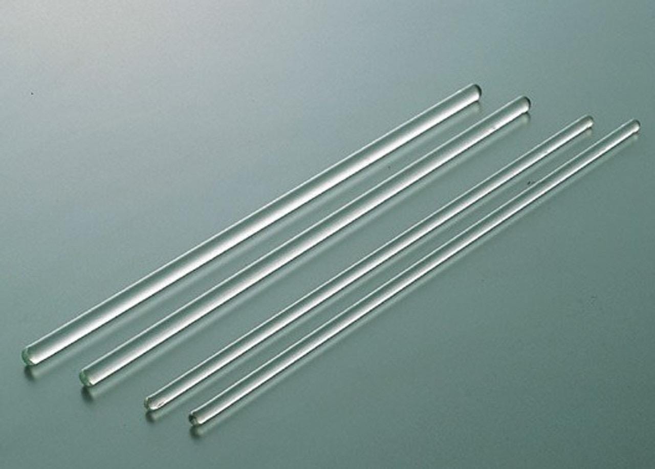 A set of three clear glass rods of varying lengths lying on a grey surface.