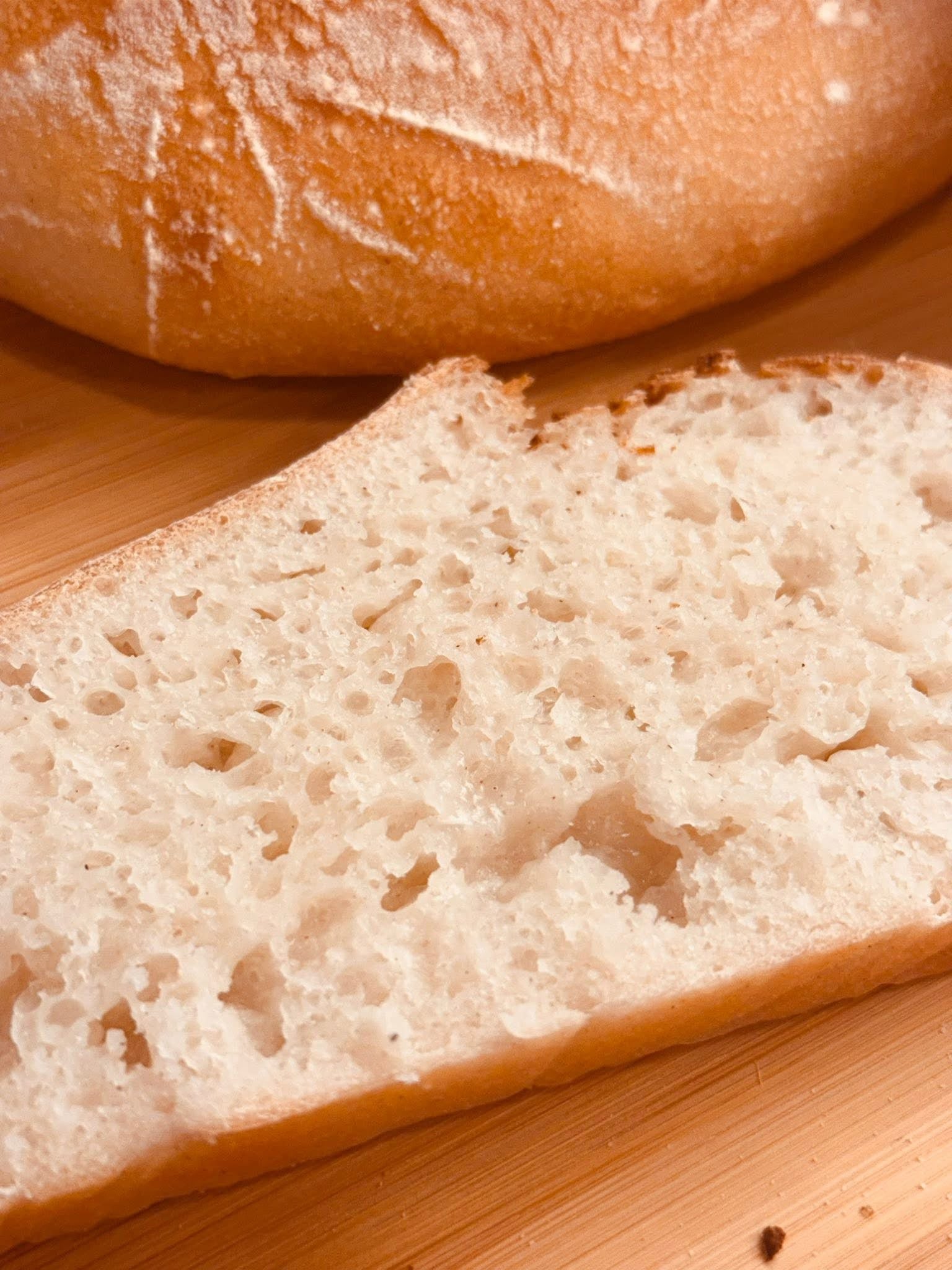 A close-up of a slice of Gluten Free bread with a focus on its porous texture, with a loaf partially visible in the background.