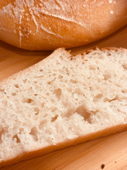 A close-up of a slice of Gluten Free bread with a focus on its porous texture, with a loaf partially visible in the background.